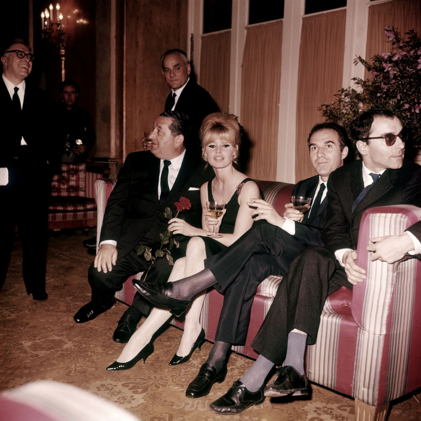 Brigitte Bardot attends the opening of Contempt in Rome with, to her left, actor Michel Piccoli and director Jean-Luc Godard. The author Alberto Moravia stands behind the couch.